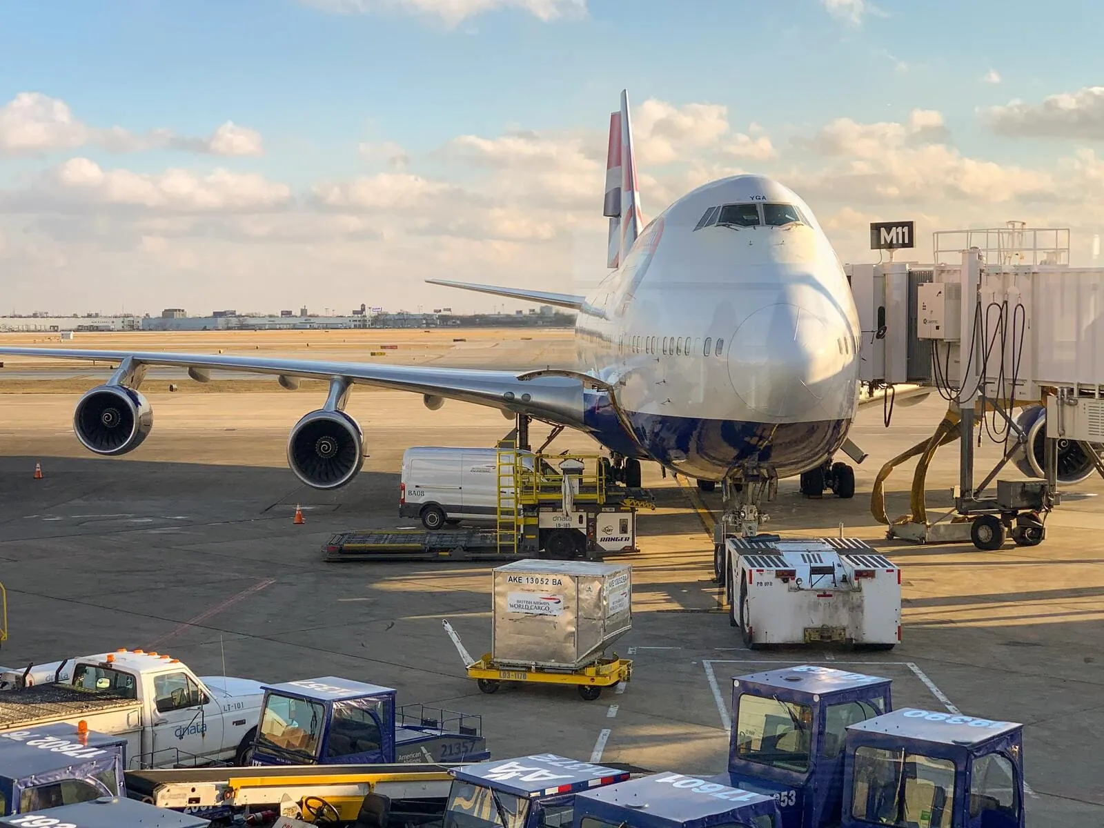 Freight aircraft on an airport apron beside cargo pallets and ground-handling vehicles.